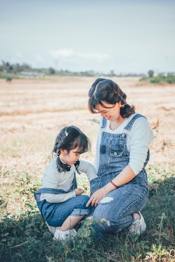 Smiling Woman and Girl Sitting on Grass Field