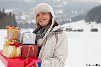 Smiling woman carrying Christmas gifts in snowy field