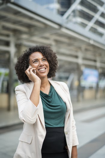 Smiling Woman Holding Phone Standing Beside Building