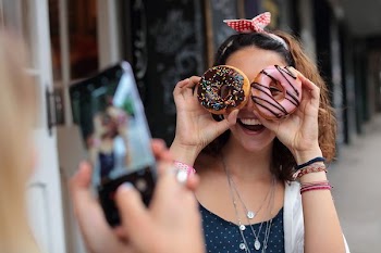 smiling woman holding two donuts near glass stall