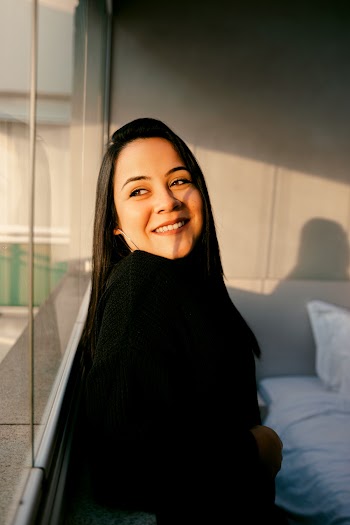 Smiling Woman in Black Sweater Standing by Glass Window