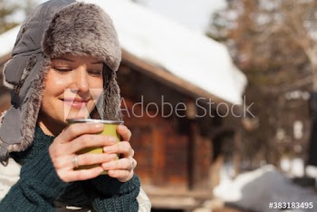 Smiling woman in fur hat drinking coffee outside cabin