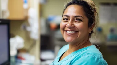 Smiling Woman in Scrubs at Computer in Healthcare Setting - PNG