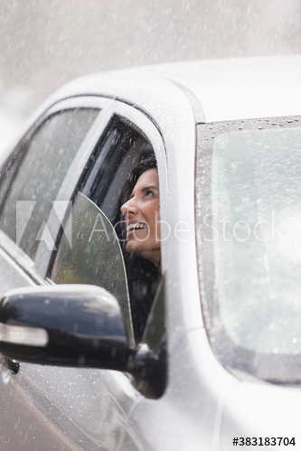 Smiling woman looking out car window at rain