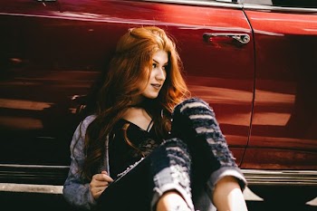 smiling woman sitting beside red car