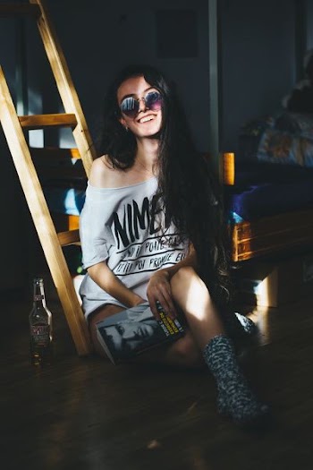 smiling woman sitting on brown wooden ladder while holding book inside room