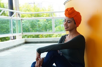 Smiling Woman Sitting On Floor And Leaning On Yellow Wall