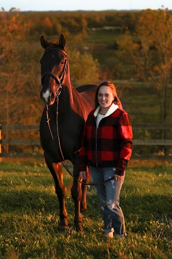 Smiling Woman Standing Beside Brown Horse on Green Grass