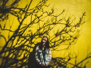Smiling Woman Standing in Front of Yellow Wall With Shadow of Leafless Tree