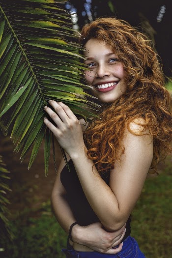 Smiling Woman Standing Near Palm Tree Holding Its Leaf