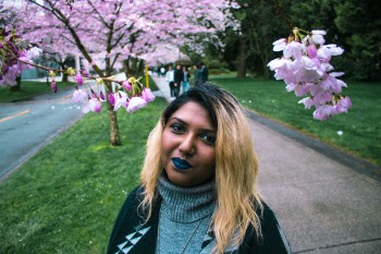 Smiling Woman Standing on Sidewalk Beside Road Near Pink Cherry Blossom Tree