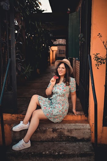 Smiling Woman Wearing a Floral Dress  Sitting on a Veranda Holding a Flower