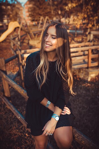 Smiling Woman Wearing Black Crew-neck Long Sleeved Midi Dress Sitting on Brown Wooden Rail