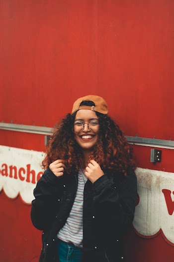 Smiling Woman Wearing Black Jacket Leaning on Red Wall