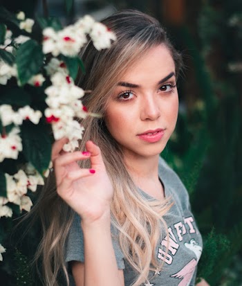 Smiling Woman Wearing Gray and Pink Shirt Touching White Petaled Flowers\