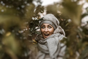 Smiling Woman Wearing Grey Coat and Cap Beside Green Plants