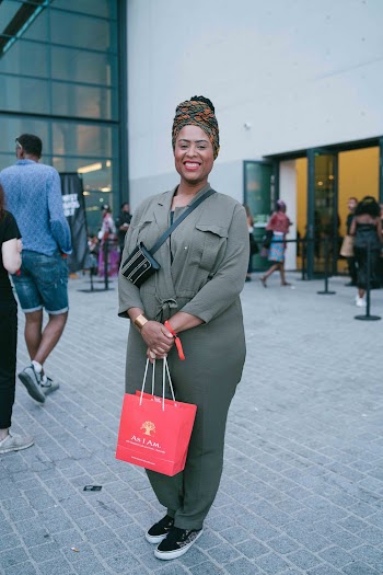 Smiling Woman Wearing Jumpsuit Holding Red Paper Bag