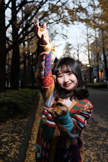 Smiling Woman Wearing Multicolored Coat Standing While Raising Right Hand on Road