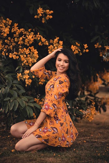 Smiling Woman Wearing Orange Dress Sitting Near Flowers