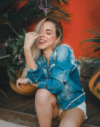 Smiling Woman While Sitting Wearing Blue Denim Button-up Jacket Beside Plants