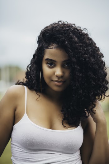 Smiling woman with curly hair wearing a white tank top