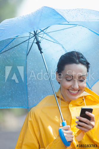 Smiling woman with umbrella using smart phone