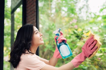 Smiling young asian woman housewife washes a window