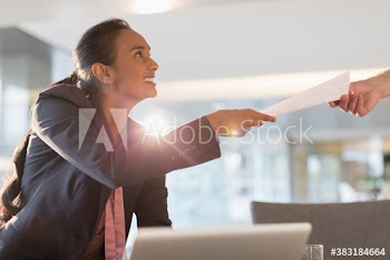 Smiling young businesswoman giving paperwork to colleague in office