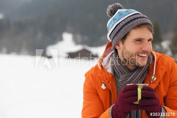 Smiling young man drinking hot cocoa in snow