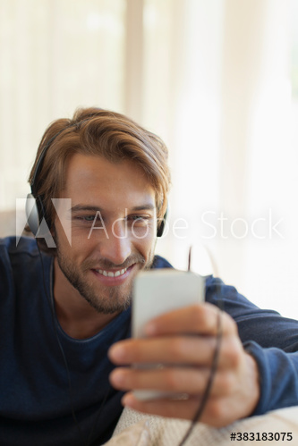 Smiling young man listening to music with headphones and smart phone