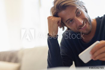 Smiling young man using smart phone on sofa