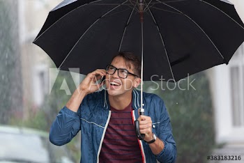 Smiling young man with umbrella talking on smart phone in rain