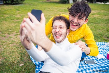 Smiling young men taking selfie while relaxing in park
