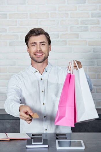 Smiling young salesman holding paper bags and credit card in shop