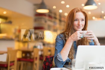 Smiling young woman drinking coffee and working at laptop in cafe