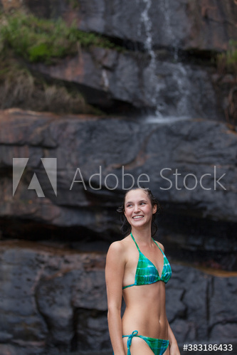 Smiling young woman in bikini below waterfall