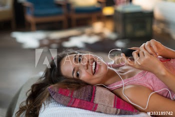 Smiling young woman listening to music on bed