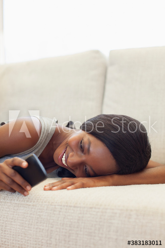 Smiling young woman relaxing on sofa with smart phone