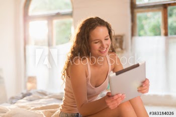 Smiling young woman using digital tablet on bed