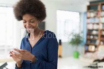 Smiling young woman with afro texting with smart phone