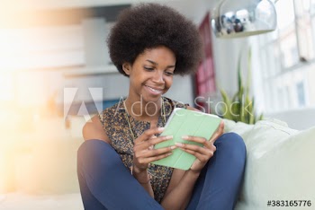 Smiling young woman with afro using digital tablet on sofa