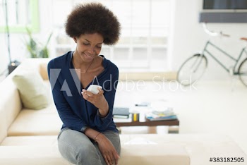Smiling young woman with afro using smart phone on sofa