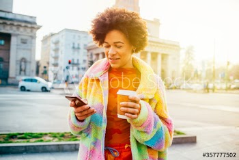 Smiling young woman with coffee cup using smartphone in city