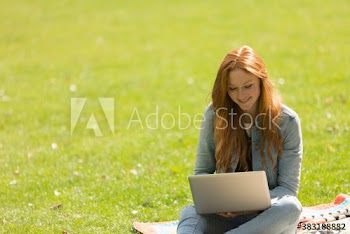 Smiling young woman with laptop in sunny park grass