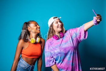 Smiling young women taking selfie while standing indoors