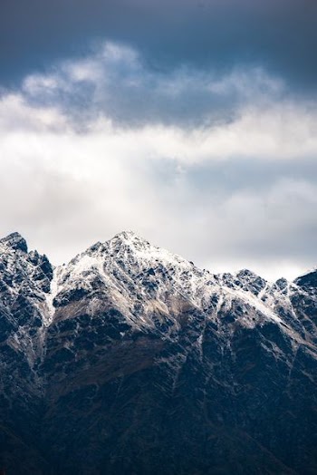 snow-capped mountain below cloudy sky