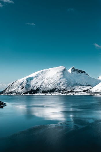 Snow Covered Mountain Near Calm Body Of Water Under Clear Blue Sky