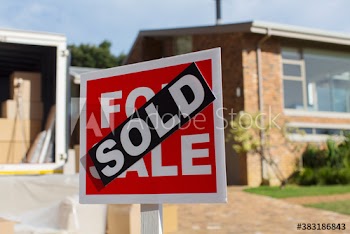 Sold sign outside house and moving van in sunny driveway