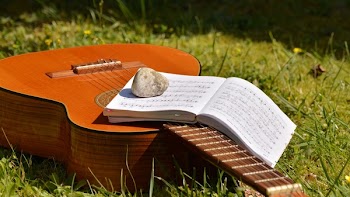 Song Book on Brown Classical Guitar on Green Grass during Daytime
