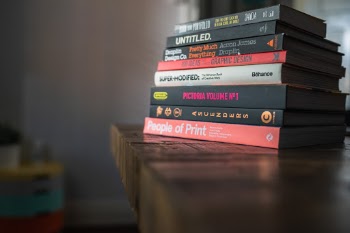 Stack of marketing and graphic design books on an old wooden oak table with light leaking in. 